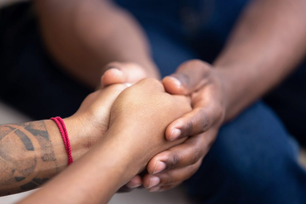 Close-up of two people holding hands in a supportive, comforting gesture.