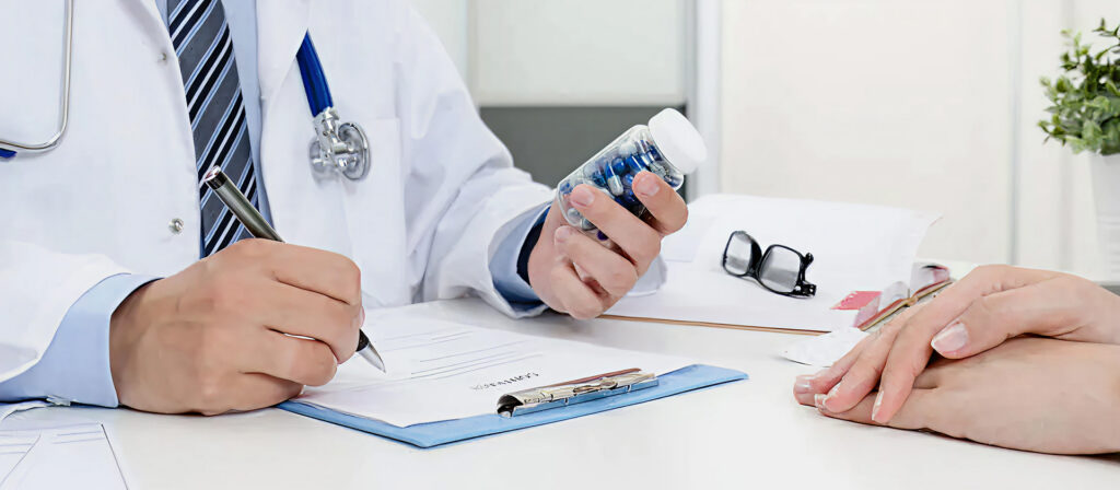 Doctor writes a prescription while holding a medication bottle as a patient rests hands on the desk.