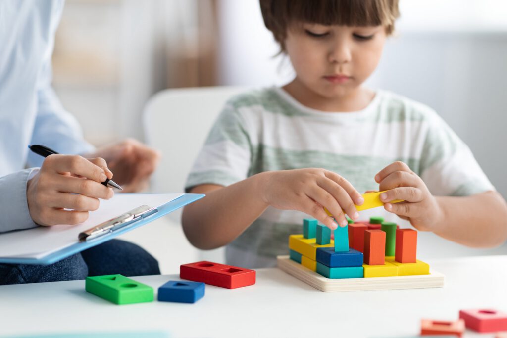 Clinician taking notes while a child plays with colorful blocks
