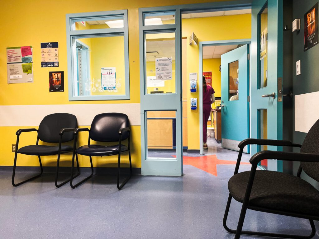 Empty clinic waiting room with chairs and open doors leading to a hallway.