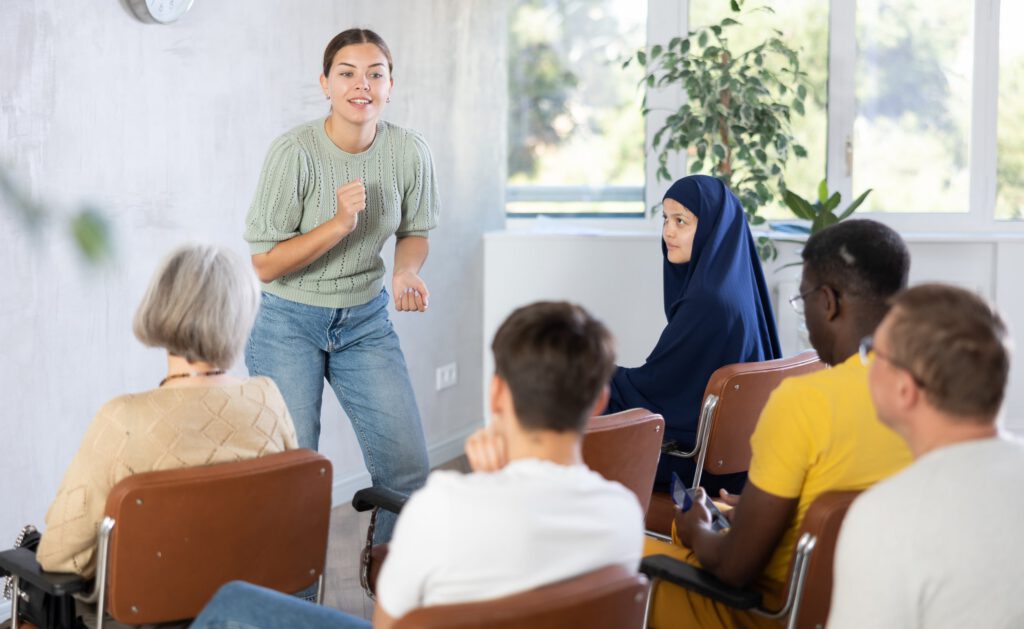 Facilitator speaking to an engaged group during a community workshop or training session.