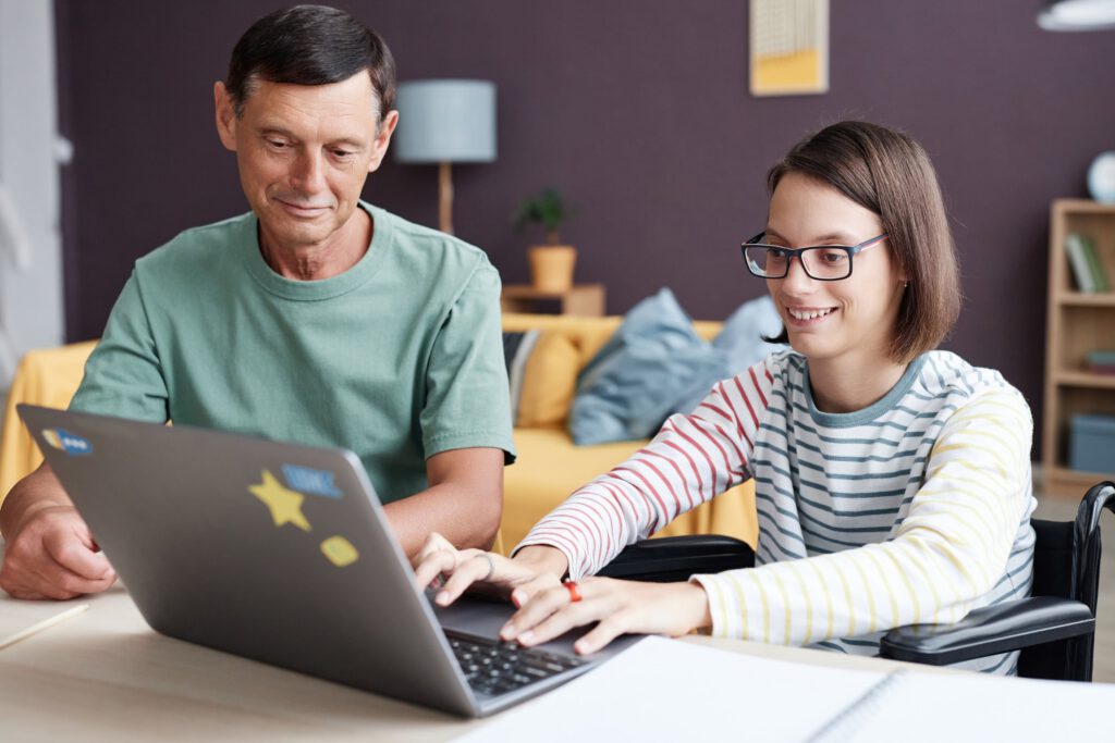Young woman in wheelchair using a laptop with caregiver support