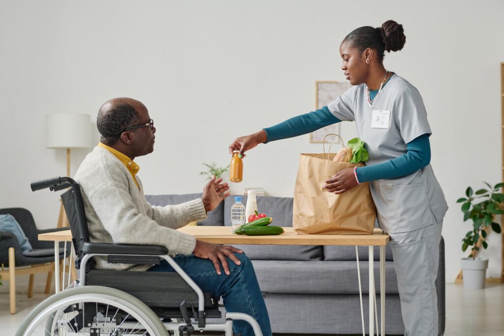 Home health aide delivering groceries to a man in a wheelchair
