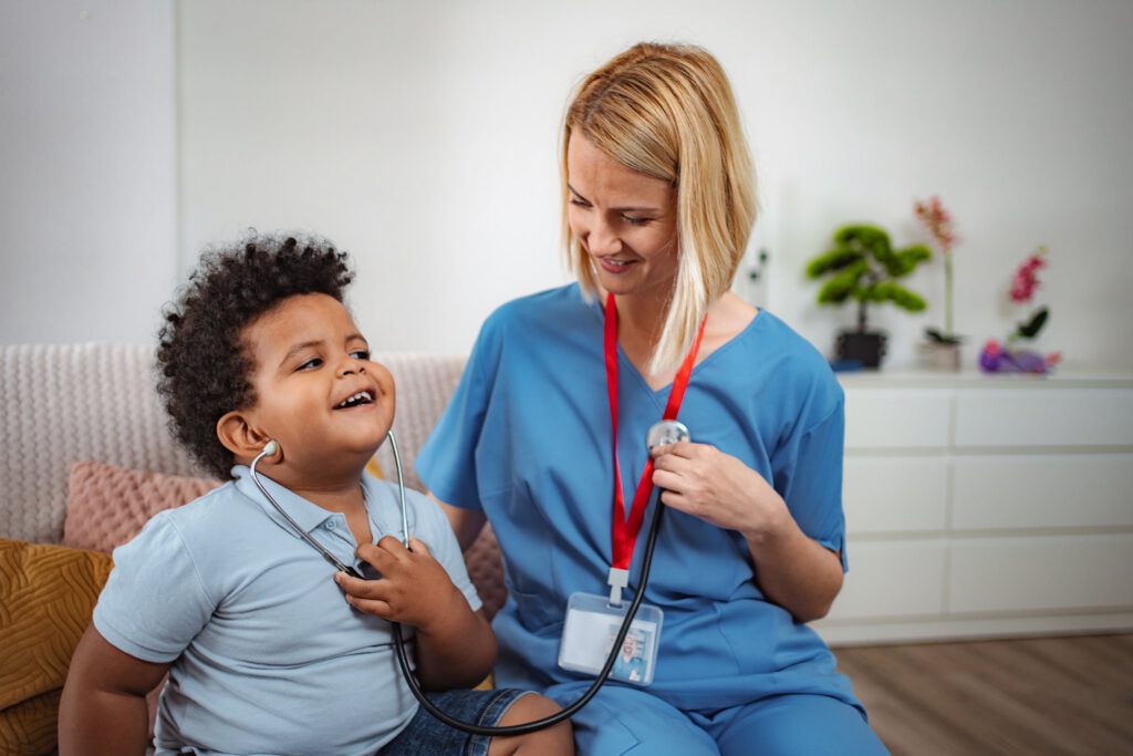 Healthcare professional using a stethoscope while a child smiles during a checkup.