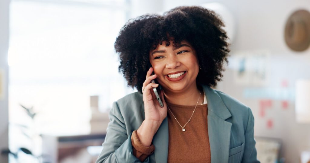Smiling professional woman talking on a phone in an office setting.