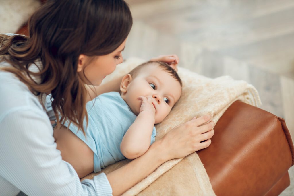 Mother gently cradles her baby on a soft blanket while sitting on a sofa