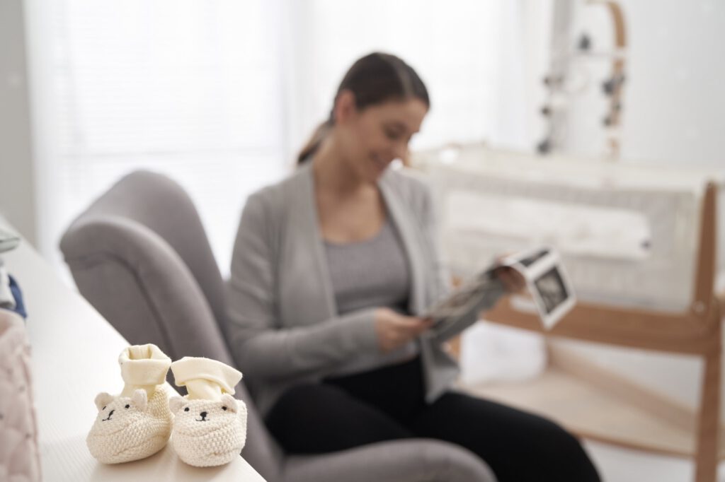 Pregnant woman holds an ultrasound image in a nursery with knitted baby booties in the foreground