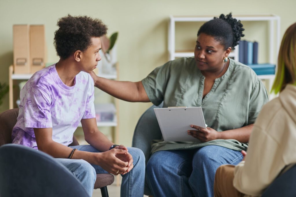 Therapist rests a reassuring hand on a teenager’s shoulder during a counseling session
