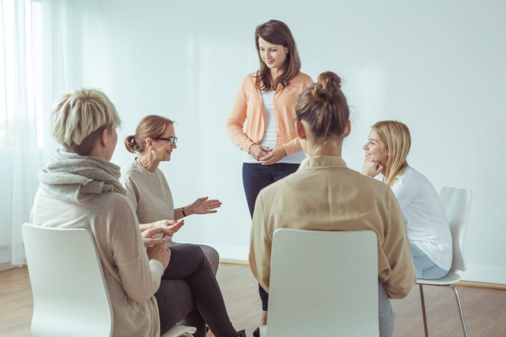 Woman standing and speaking during a small support group meeting in a bright room